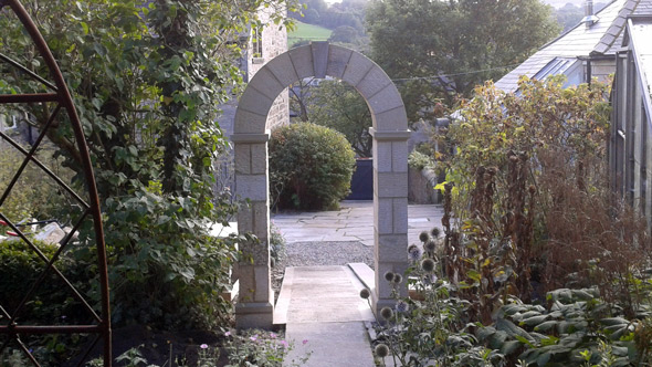 stone archway from garden overlooking paved patio surrounded by garden shrubbery