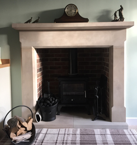 stone fireplace and black traditional fire in livingroom with clock on mantelpiece and wood chippings in black metal basket