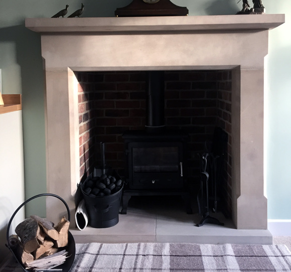 stone fireplace and black traditional fire in livingroom with clock on mantelpiece and wood chippings in black metal basket