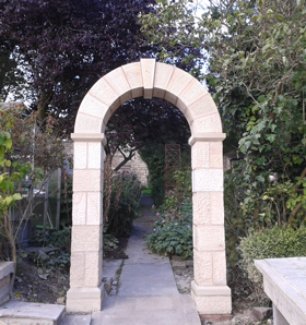 stone archway in garden surrounded by trees with a stone slab path leading away