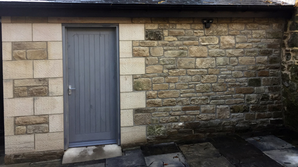 grey wooden door built into stone wall of outhouse